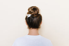 Glossy white TopBun hair clip shown holding a high bun in brunette hair